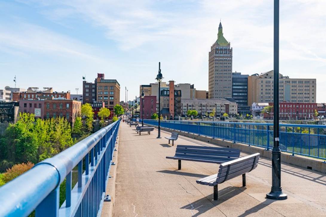 A blue railing over a bridge with benches and buildings in the background

AI-generated content may be incorrect.